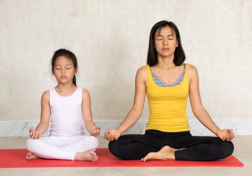 asia woman and her charming little daughter do yoga Beautiful young asia woman and her charming little daughter are smiling while doing yoga together at home